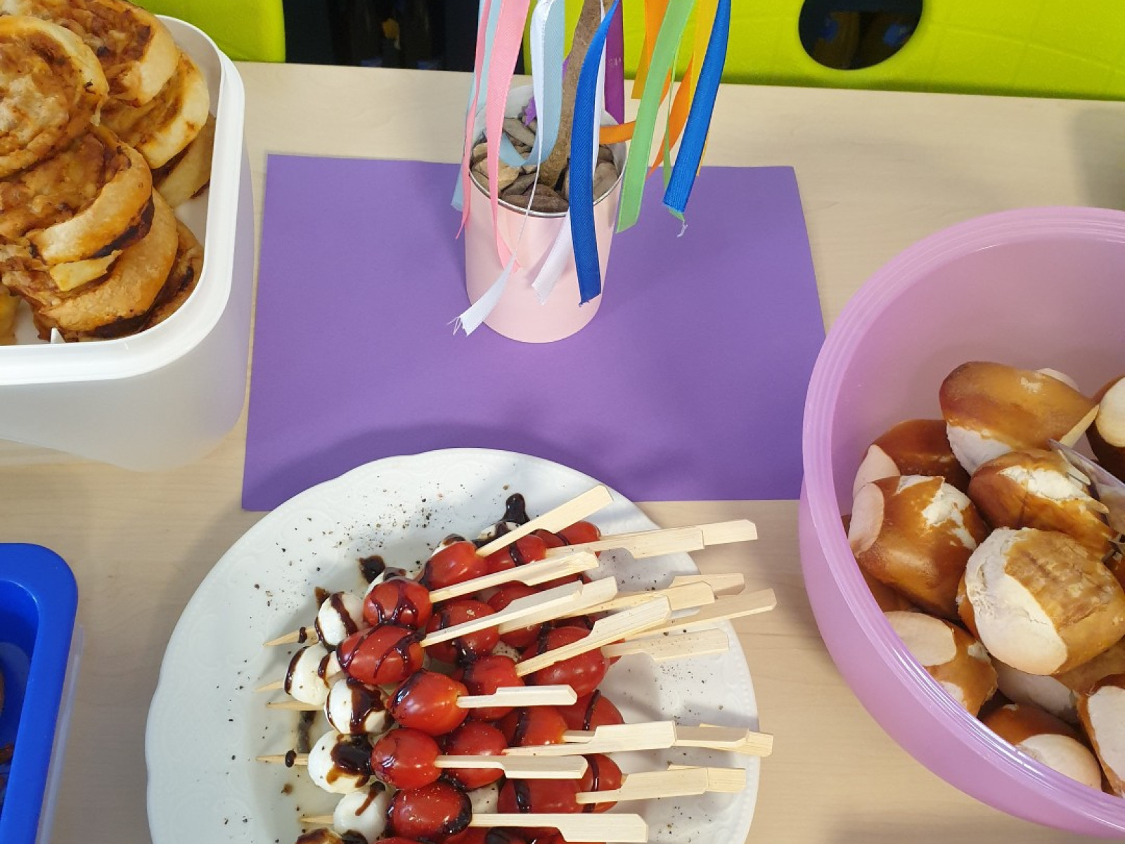 Tisch mit Caprese-Spießen, Brezeln, einer Tischdekoration aus Papier und weiteren Snacks.