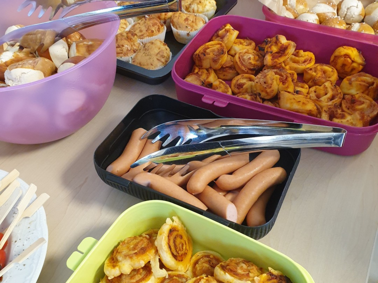 Ein Buffet-Tisch mit verschiedenen Schüsseln und Platten voll mit Snacks wie Würstchen und Blätterteigschnecken.
