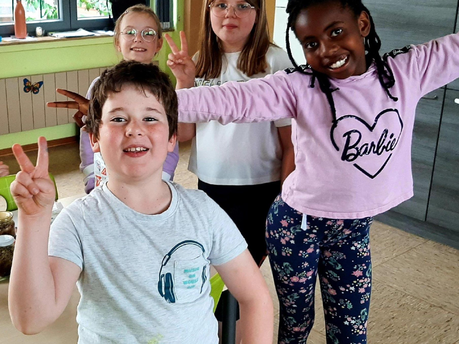 Vier Kinder stehen zusammen in einem Raum und zeigen freudig das Peace-Zeichen.