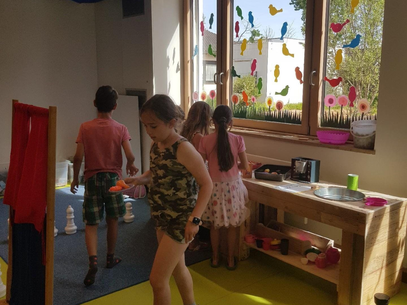 Kinder spielen in einem Raum mit großen Schachfiguren und bunten Fensterdeko.