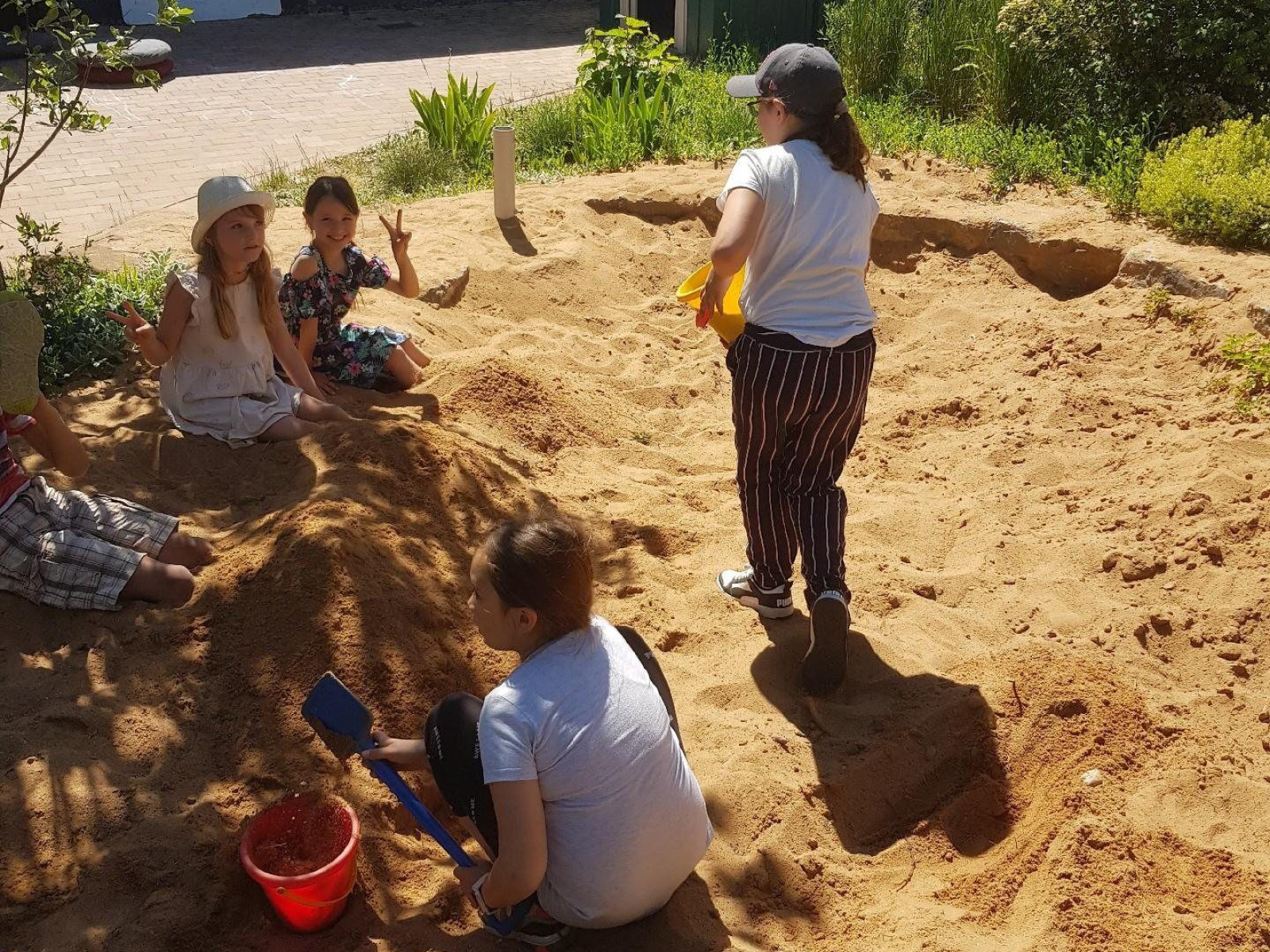 Mehrere Kinder spielen zusammen in einem Sandkasten unter strahlendem Sonnenschein.