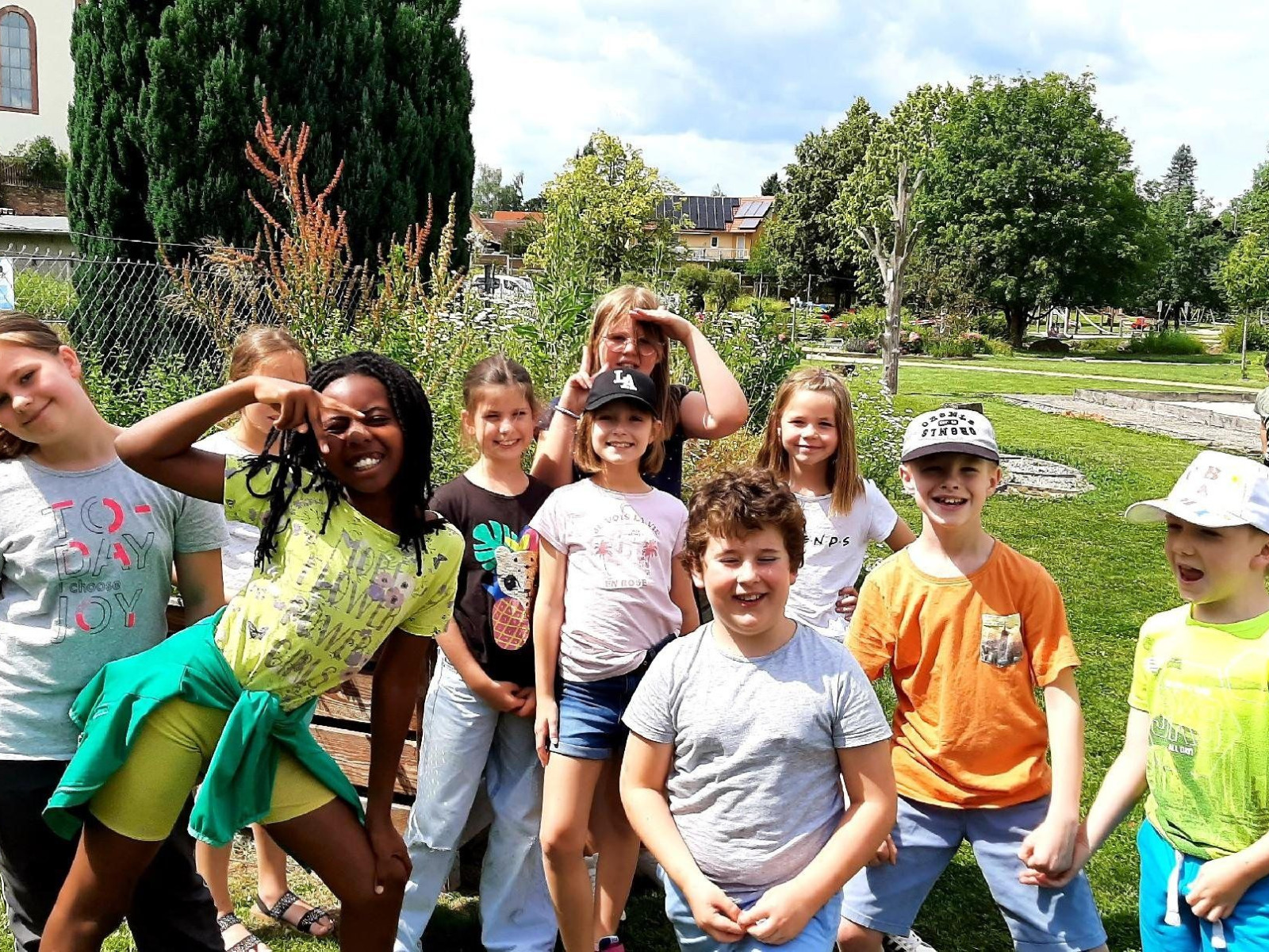 Lachende Kindergruppe im Freien auf einer grünen Wiese.