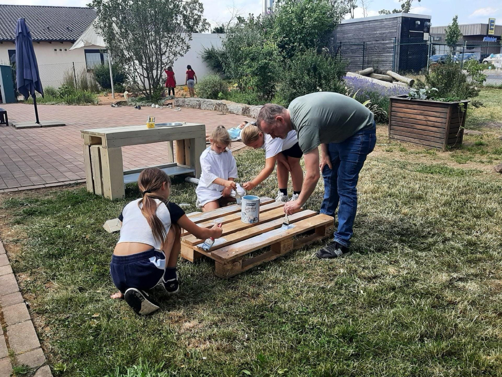 Vier Personen bemalen im Freien eine Holzpalette als gemeinsames Projekt.