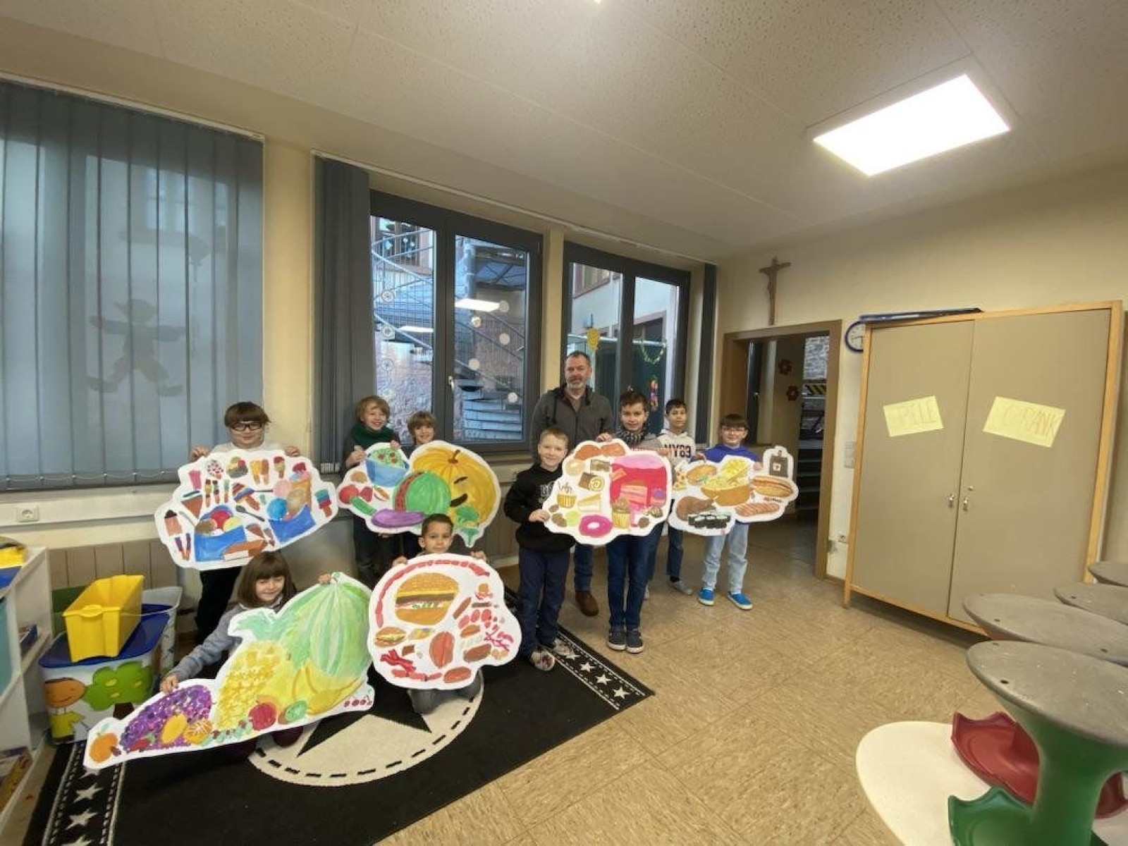 Kinder zeigen ihre Papierkunstwerke in einem Klassenzimmer, fröhlich posierend.