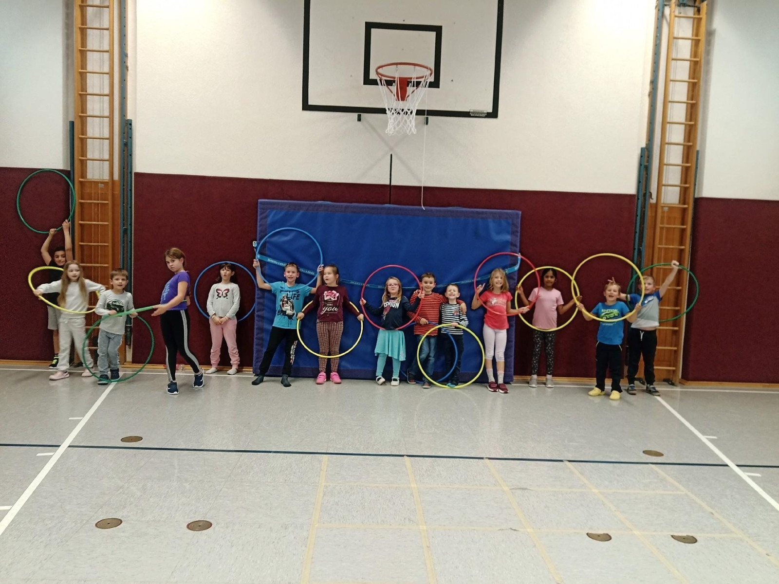 Kinder stehen in einer Turnhalle mit Hula-Hoop-Reifen vor einem Basketballkorb.