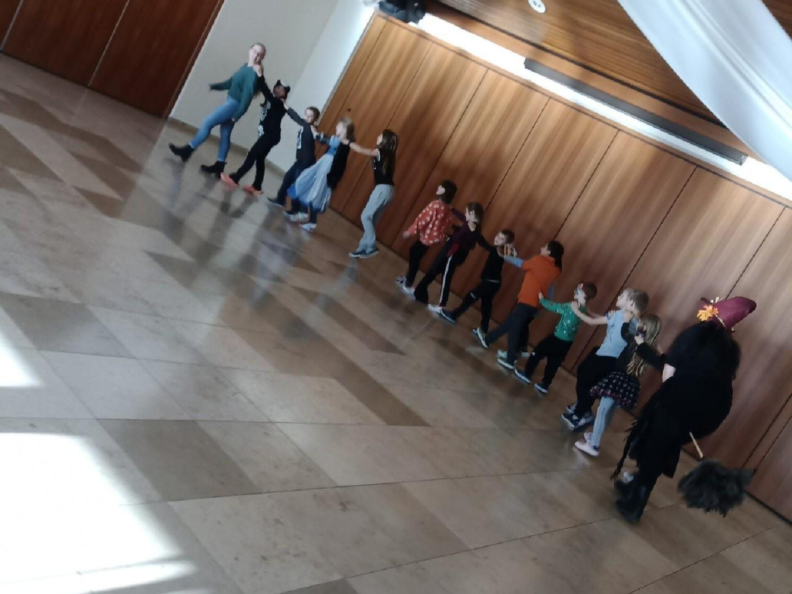 Gruppe von Kindern tanzt in einer Linie in einem großen Raum mit hölzernen Wänden.