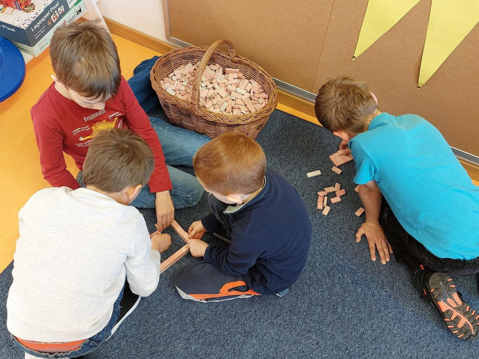 Vier Kinder sitzen auf dem Teppich und spielen mit einer Sammlung von Holzklötzen aus einem Korb.