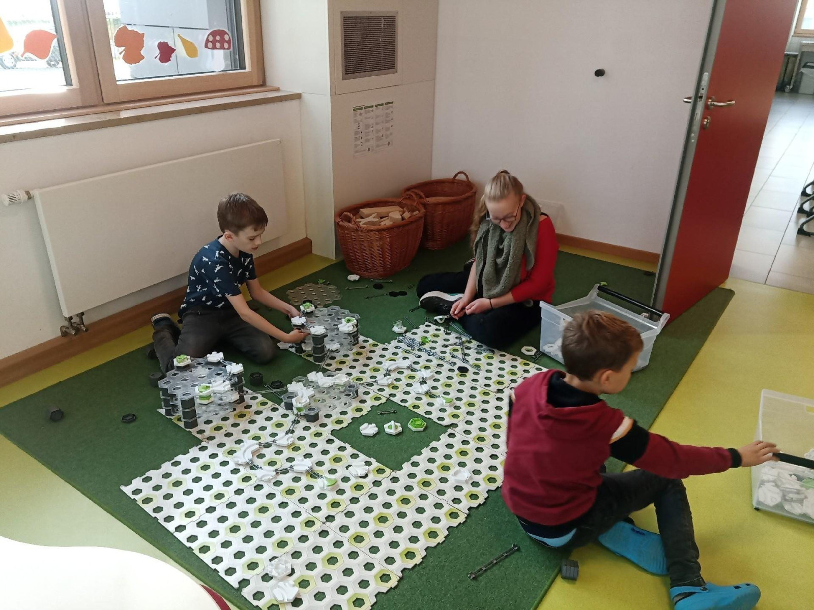 Drei Kinder sitzen auf grünem Teppich im Raum und bauen mit Bauklötzen.