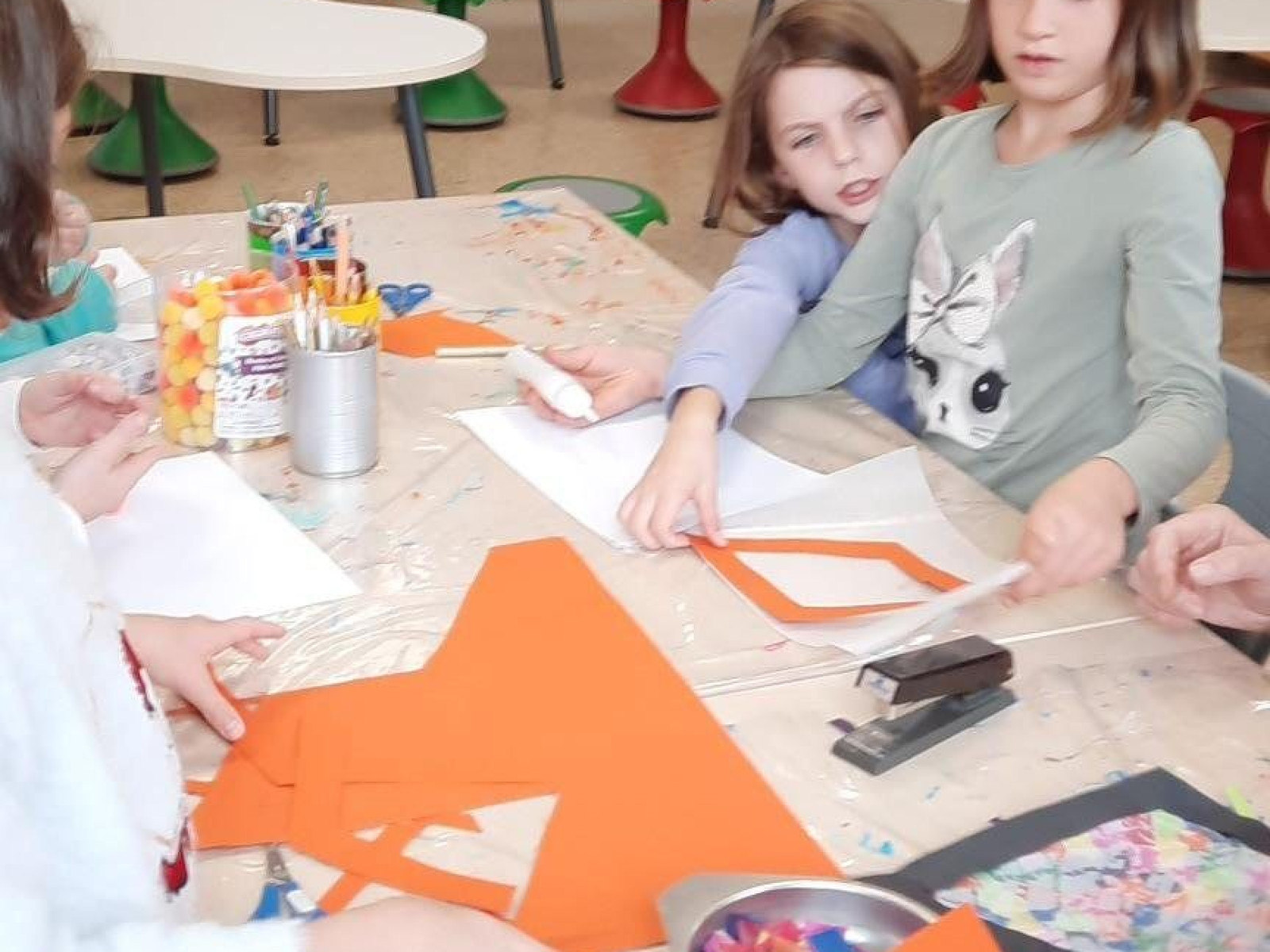 Kinder basteln im Klassenzimmer mit buntem Bastelpapier und Zubehör auf einem Tisch.