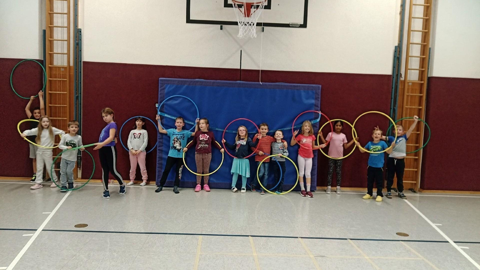 Eine Gruppe von Kindern in einer Sporthalle, die Hula-Hoop-Reifen halten.